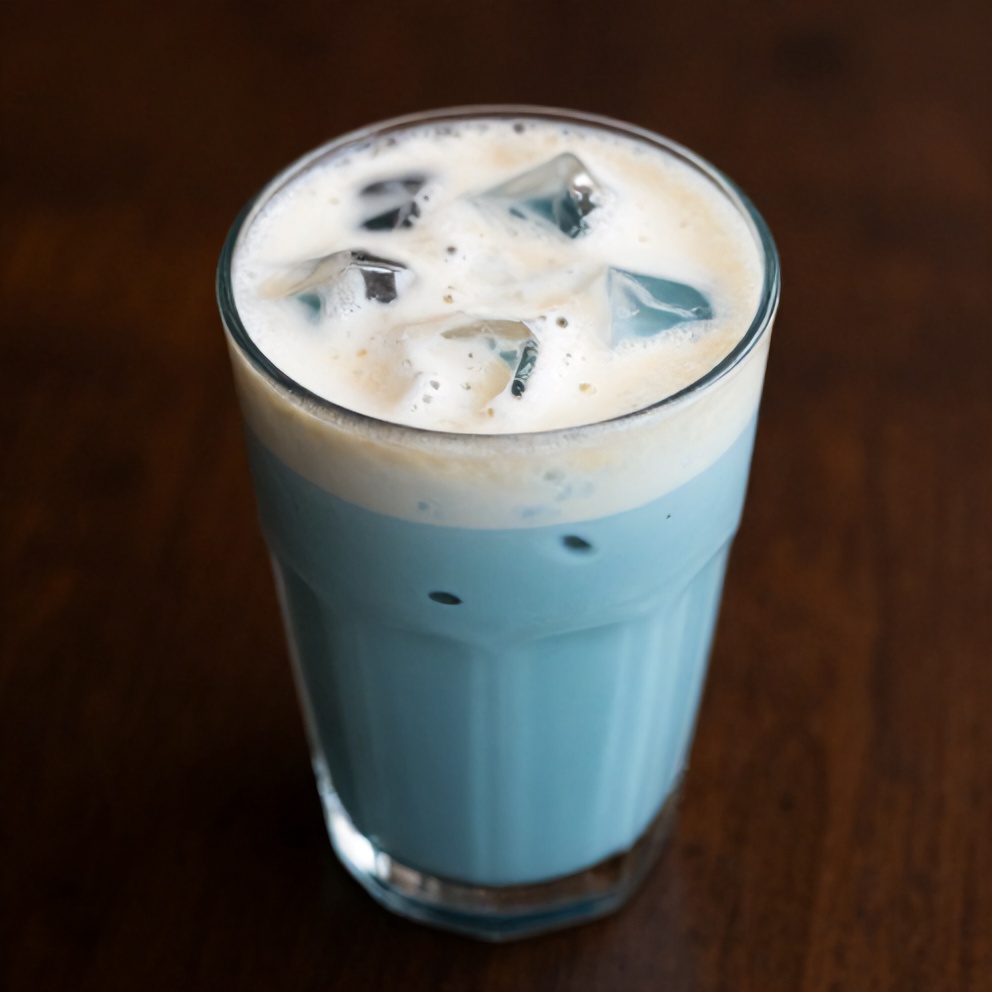Iced blue tea latte with vanilla cold foam garnished with a lemon slice